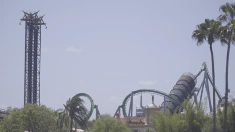 Epic-shot-of-a-roller-coaster-shooting-out-of-a-tunnel-through-twists-and-turns,-while-people-nearby-are-launched-up-a-large-tower-ride