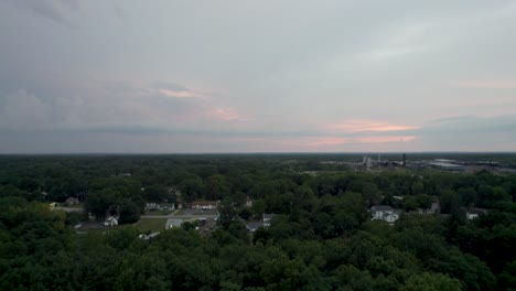 Drone-shot-over-small-town-surrounded-by-green-vegetation-along-rural-countryside-during-evening-time