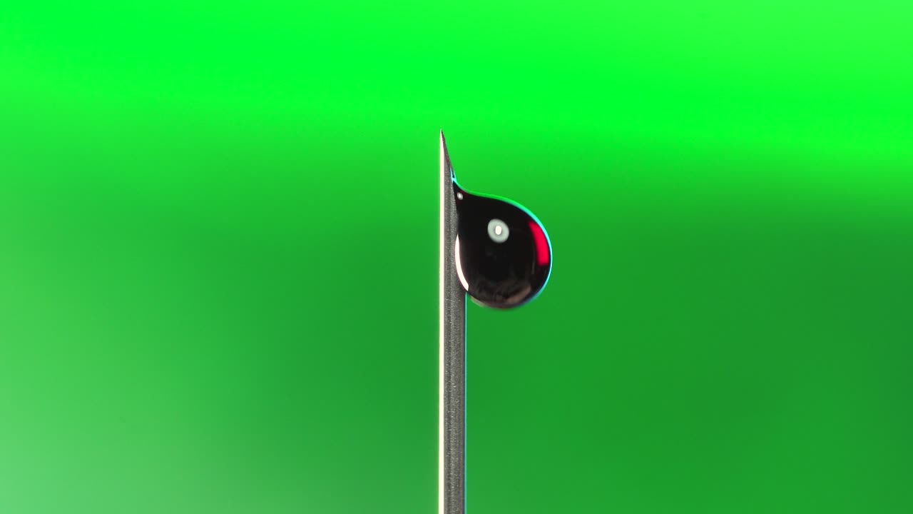 Macro extreme close up blood droplet from hypodermic needle on green background