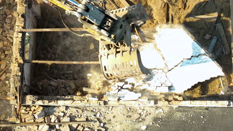 overhead shot showing an excavator claw breaking through a wall, reducing it to rubble on a construction site