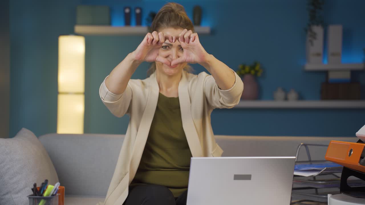 Home office worker woman makes heart symbol looking at camera.