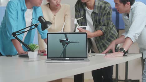 테이블 위의 노트북은 아시아 엔지니어 그룹이 사무실에서 작업에 대해 논의하는 동안 풍력 터빈의 비디오를 보여주고 있습니다.