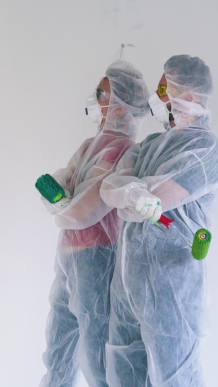 Dolly cam: man and woman in protective suits and masks displeased of green paint strokes on white wall in renewing room