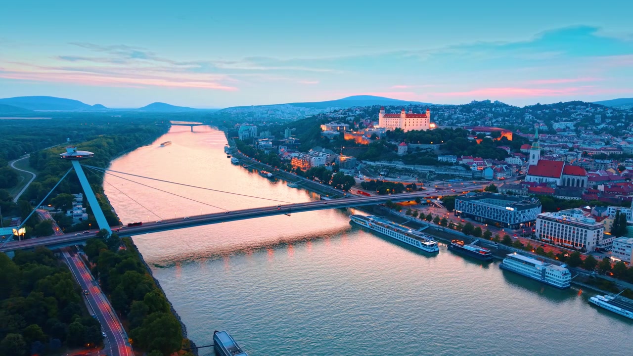 Højt vinkelperspektiv af Bratislava Slot og Most SNP. Solnedgangslys farver himlen over Donau-floden og historisk byarkitektur