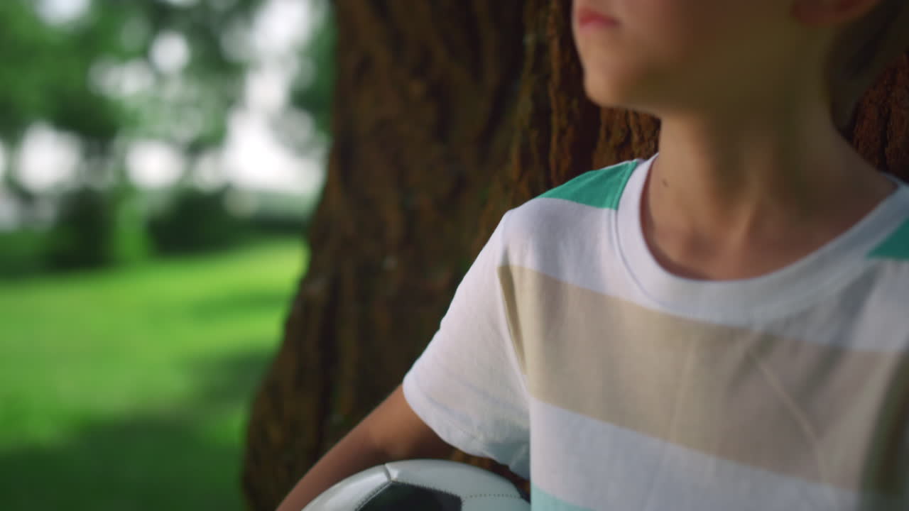 retrato de un niño sosteniendo una pelota cerca de un árbol. un niño posando con una pelota de fútbol en el parque.