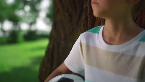 ritratto di un ragazzo che tiene la palla vicino a un albero. un bambino che posa con una palla da calcio nel parco.