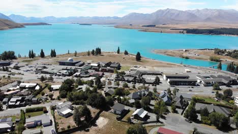 Aerial-View-of-Idyllic-Lake-Tekapo-Village,-New-Zealand-on-Sunny-Day,-Blue-Water-and-Scenic-Coastline,-Drone-Shot