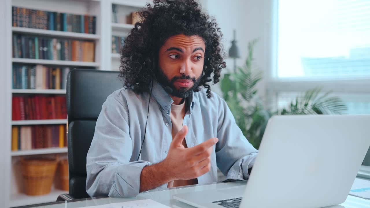 Young african american man with headset on head talking video link in laptop