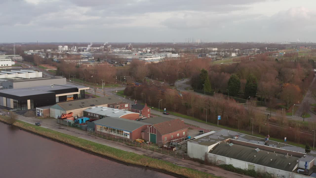 A passenger train leaving a city through an industrial zone. Drone shot