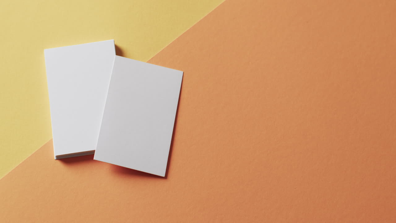 Overhead view of blank white business cards on yellow and orange background, copy space, slow motion