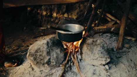 feeding a wood fire under metal bowl to roast coffee beans - african person
