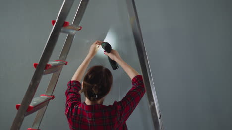 woman fastens screw in wall using automatic screwdriver