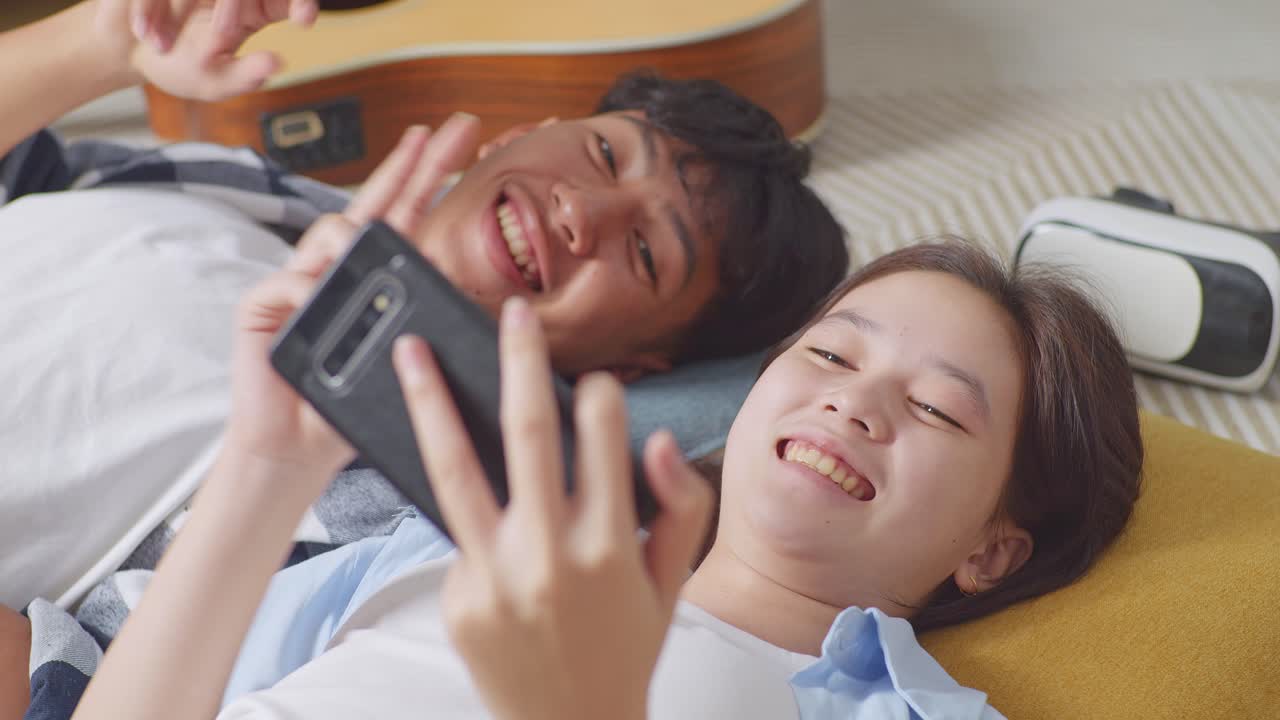 집 바닥에 카 위에 누워서 셀피를 찍는 스마트폰을 사용하는 아시아 십대 커플의 근접 사진.