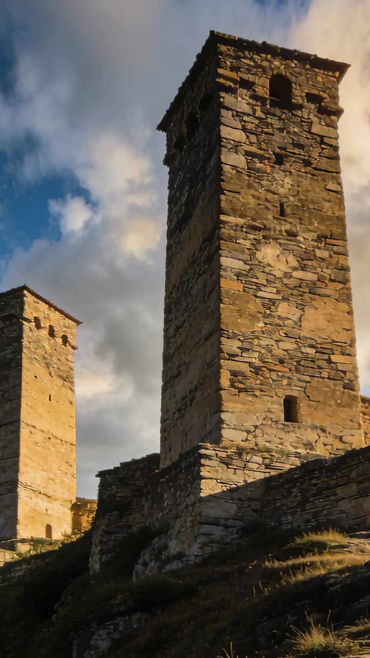 Vertical video: Clouds moving, camera tilting, revealing tall stone tower and upper sky on hillside
