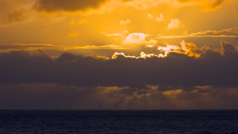 nubes oscuras que se extienden a lo largo del horizonte con turbinas eólicas giratorias mientras el sol se pone oscuro en la noche de verano