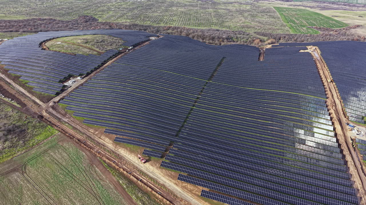 Stor solcellepark i landområde, der genererer vedvarende energi i dagtimerne med flere rækker solpaneler opstillet på marken