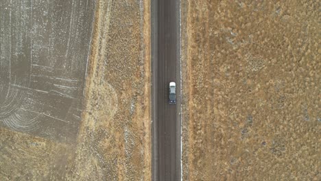 an aerial shot of a truck driving along a dirt road in central usa with fields alongside