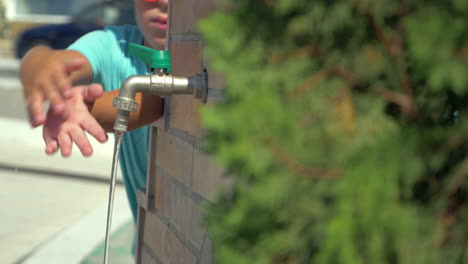 Boy-washing-hands-at-street-tap