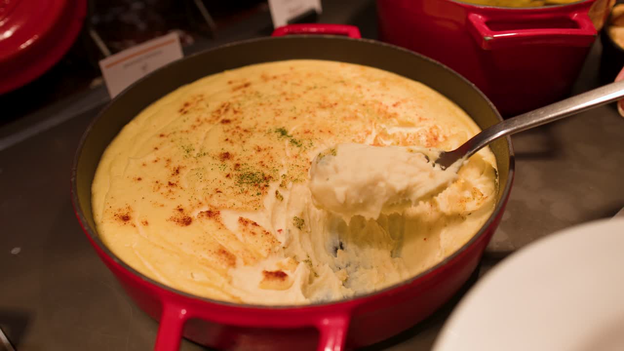 Un cucchiaio di metallo raccoglie purè di patate cremoso condito con paprika da una pentola da buffet rossa
