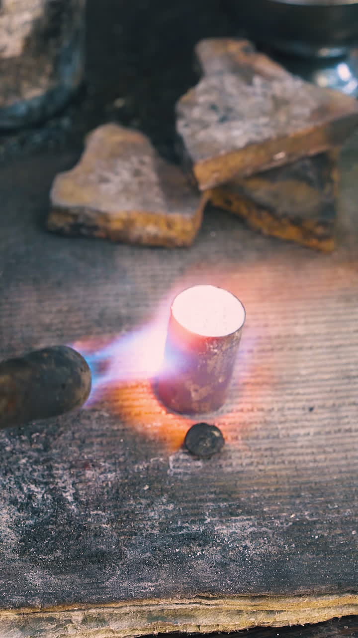 CU shot: skilled worker heats cylindrical metal bar with hot gas burner on large asbestos sheet in dark workshop closeup