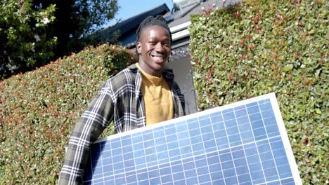 portrait of happy african american man holding photovoltaic panel entering property, slow motion