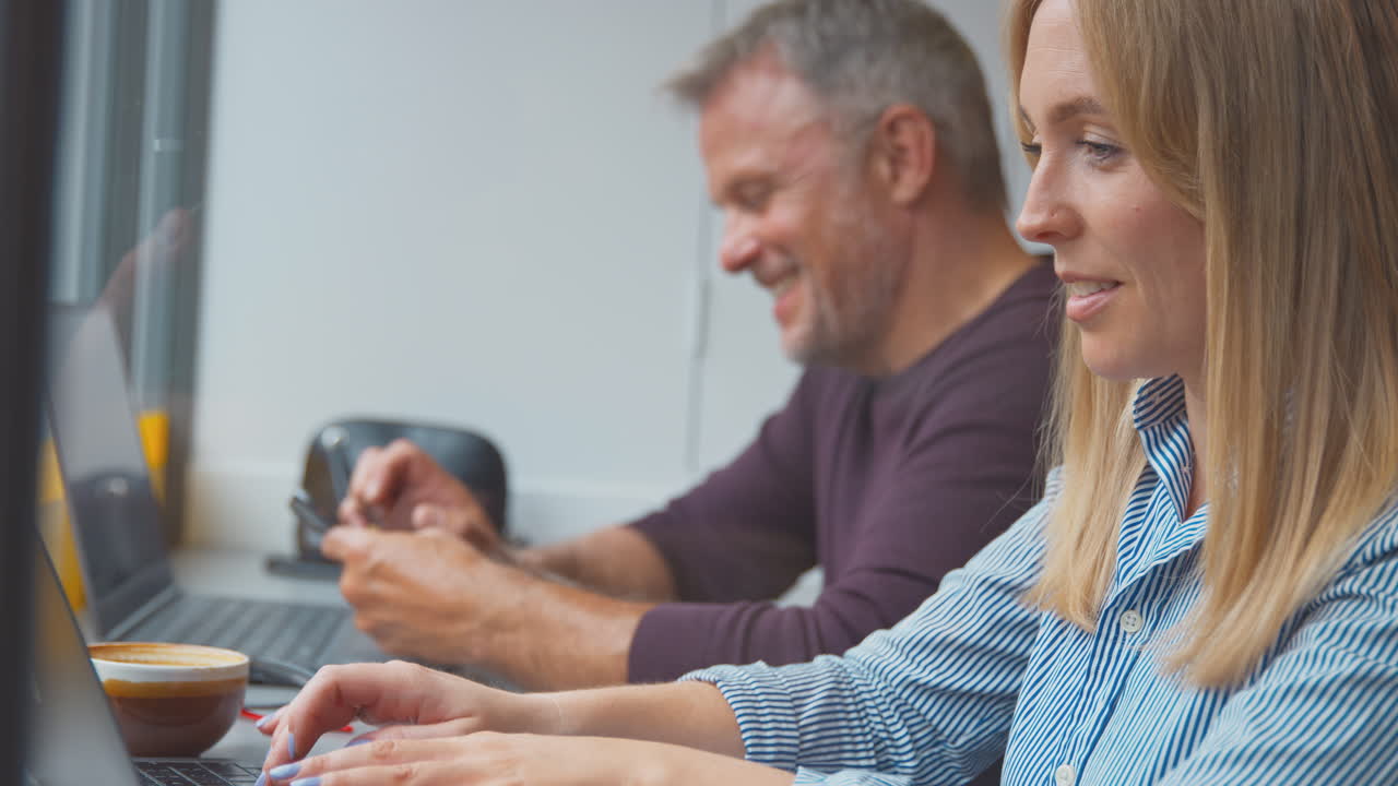 clientes en la ventana de la cafetería trabajando en computadoras portátiles y navegando en teléfonos móviles