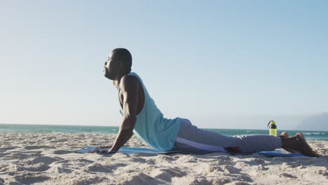 hombre afroamericano enfocado practicando yoga en la playa, haciendo ejercicio al aire libre junto al mar