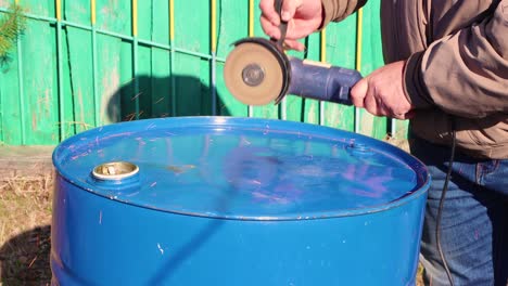 hands with an angle grinder cut a metal barrel close-up.