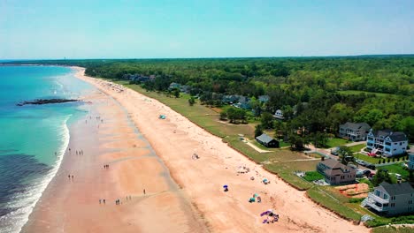 drone aerial shows saco, maine beach alive with crowds. sunlight dances on waves as people enjoy the sand near vacation homes. a perfect east coast summer day with nature, ocean, and travel fun.