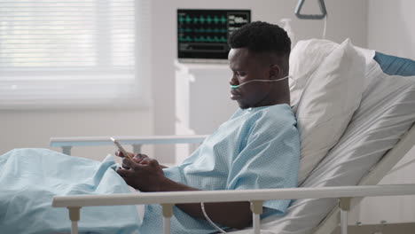 african male patient using smart phone while lying on bed. african patient having phone conversation in hospital room