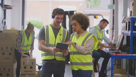 trabajadores masculinos y femeninos que usan auriculares en el almacén de distribución logística utilizando una tableta digital