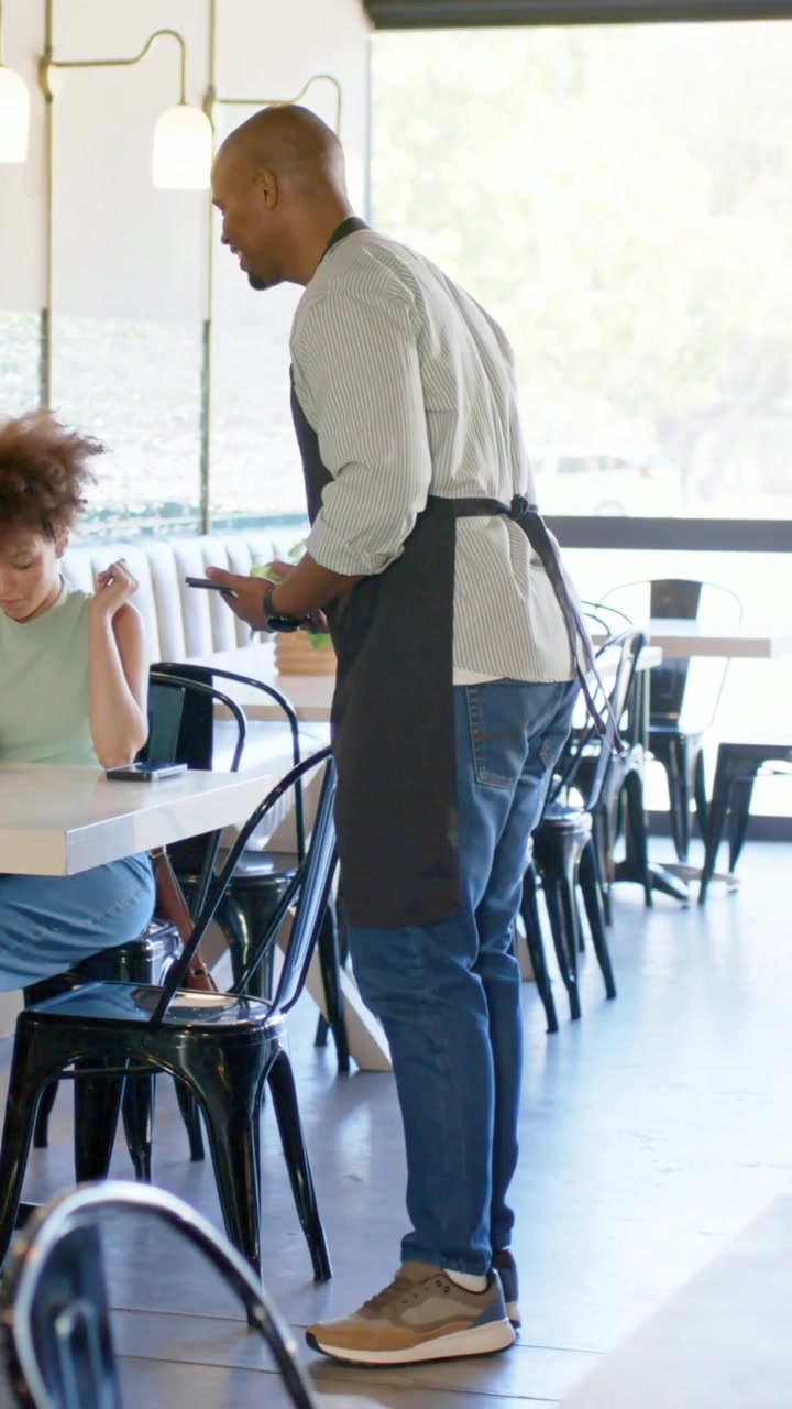 Video verticale: Cameriere che cammina con grembiule e telefono al punto di ritiro che controlla l'ordine, consegnando una tazza nel bar
