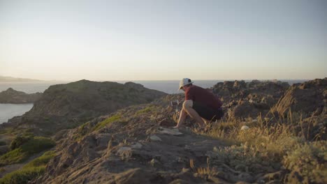 adventurer filming on the cliff with his phone, landscape, ocean in the background, sunset, static shot