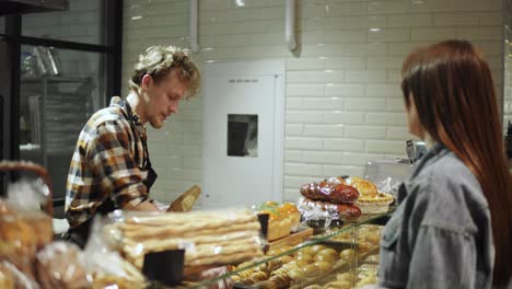 vendedor de pan empaquetando baguette fresca para una joven cliente en la hermosa tienda con productos de panadería