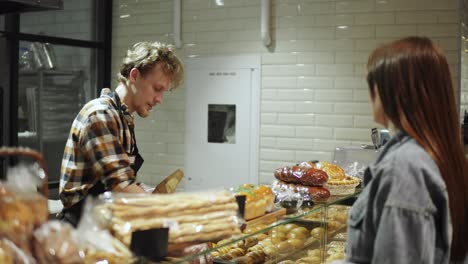 bread seller packing fresh baguette for young woman customer in the beautiful store with bakery products