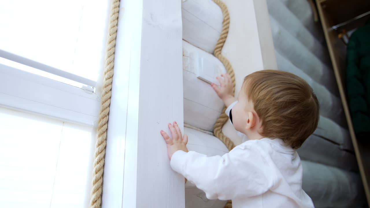 Small blond baby boy in white shirt tries to reach a light switch. Happy kid plays with the light.