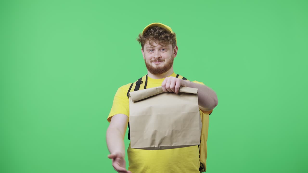 카메라를 바라보며 종이 봉지를 들고 있는 젊은 남성의 초상화. 녹색 화면에 포즈를 취하는 테르모 봉투와 함께 노란색 배달 택배 유니폼을 입은 은 머리 남성 59.97fps