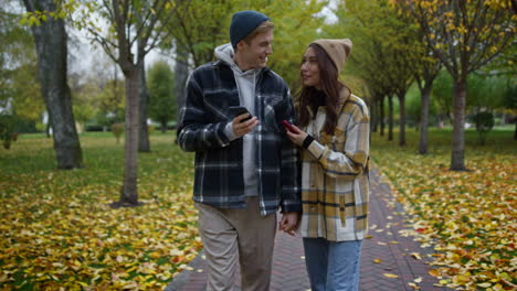 smiling young couple looking smartphones in autumn park