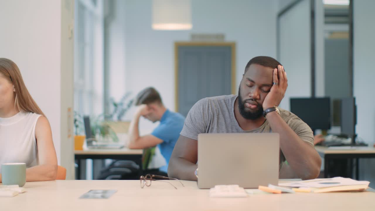 Tired man feeling sleepy at coworking. Portrait of black man falling asleep