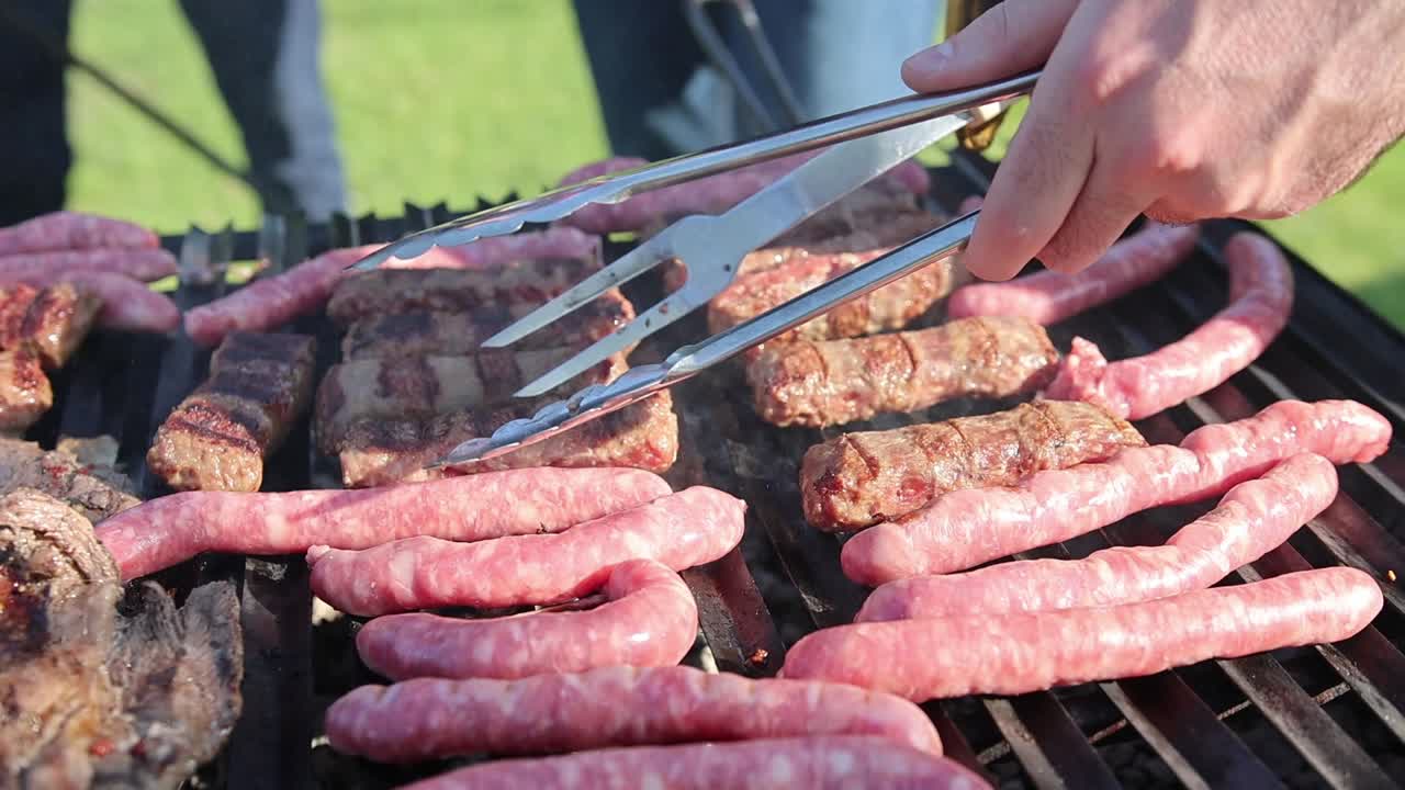 personas asando salchichas en la parrilla usando tenedor y pinzas