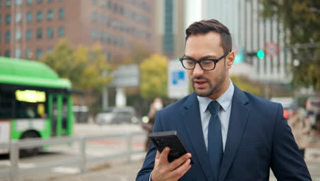 cheerful businessman communicates online using mobile phone on the move in busy city street with lively traffic