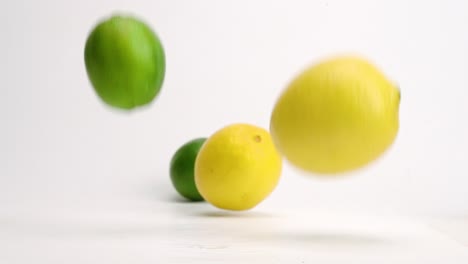 frutas cítricas enteras de limón y lima cayendo sobre la mesa blanca y rebotando y rodando en cámara lenta