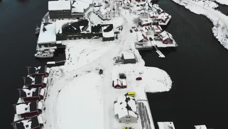 red houses and boats at the port on a snowy landscape with the mountains at the background during the winter time in norway