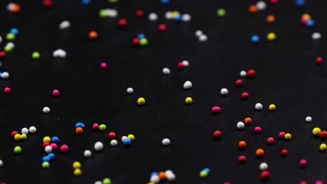a variety of colorful sprinkles are scattered randomly across a dark background, creating a lively and playful pattern.