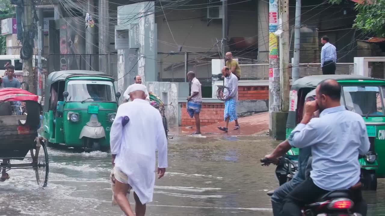 During the Monsoon Season, People and Motorists Navigate Flooded Roads While Rickshaws Pass Through the Waterlogged Streets in Bangladesh, South Asia - Handheld Shot