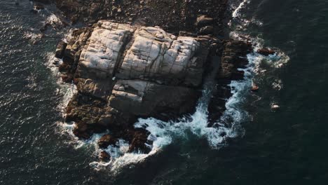 Luz-Del-Sol-De-La-Mañana-En-La-Costa-Rocosa-Rodeada-Por-Un-Océano-Azul-Oscuro-Con-Olas-Salpicando-En-Gloucester,-Massachusetts---Drone-Aéreo