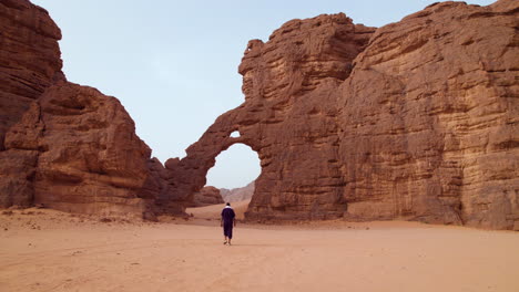 man walking in the desert at tassili n'ajjer national park towards the elephant-shaped rock formation in algeria