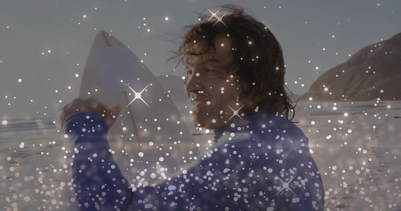 Vertical video: Sun glaring causing surfer shielding eyes, holding board on beach, wetsuit, sparkle