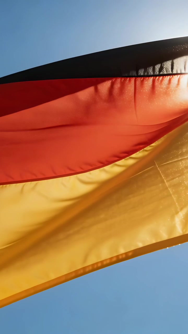Video verticale: Bandiera nero-rosso-oro che sventola a raffiche sull'asta, ondeggiando contro il cielo blu.