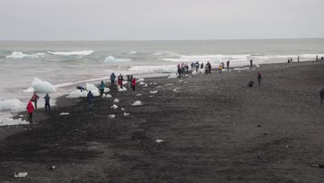 Laguna-Glaciar-En-Islandia-Con-Gente-En-La-Playa-De-Arena-Negra-Mirando-Trozos-De-Hielo